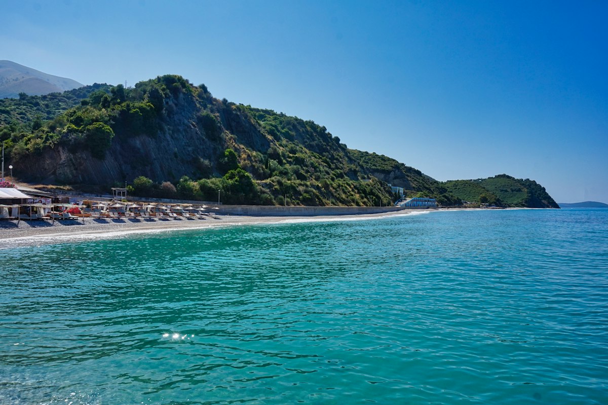 Turquoise bay on the Albanian Riviera with a pebble beach, sun loungers and green mountains dropping into the sea
