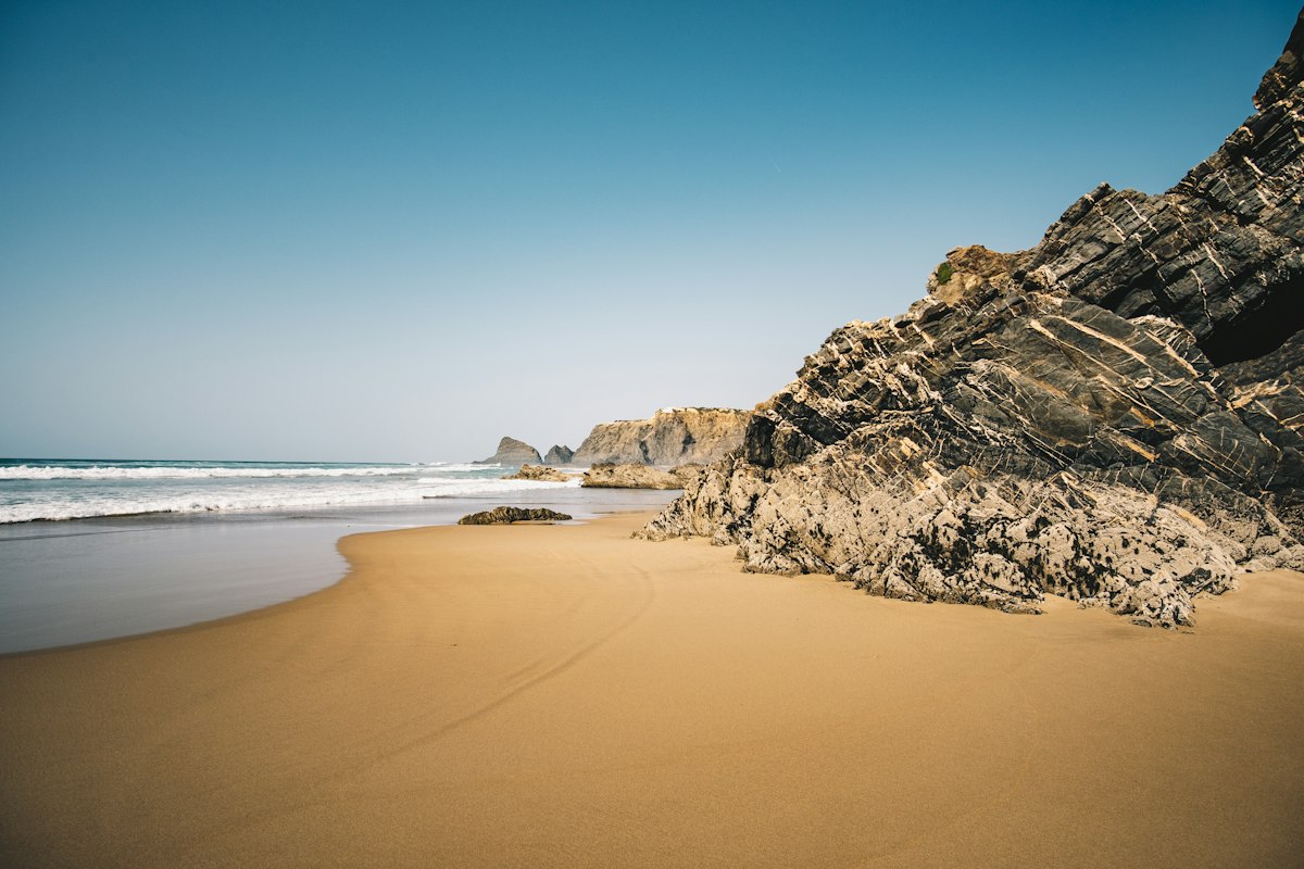 Sandy beach below a dark rocky cliff on the Algarve coast with Atlantic surf rolling in