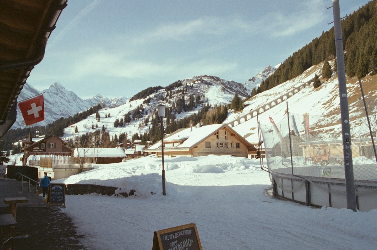 Snow covered alpine village with wooden chalets, an outdoor ice rink and mountains rising behind it