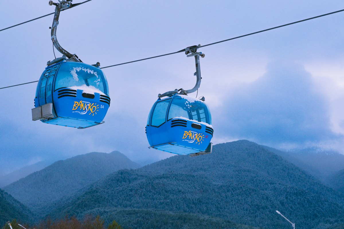 Two blue gondola cabins climbing above snow covered pine forest toward a mountain ridge