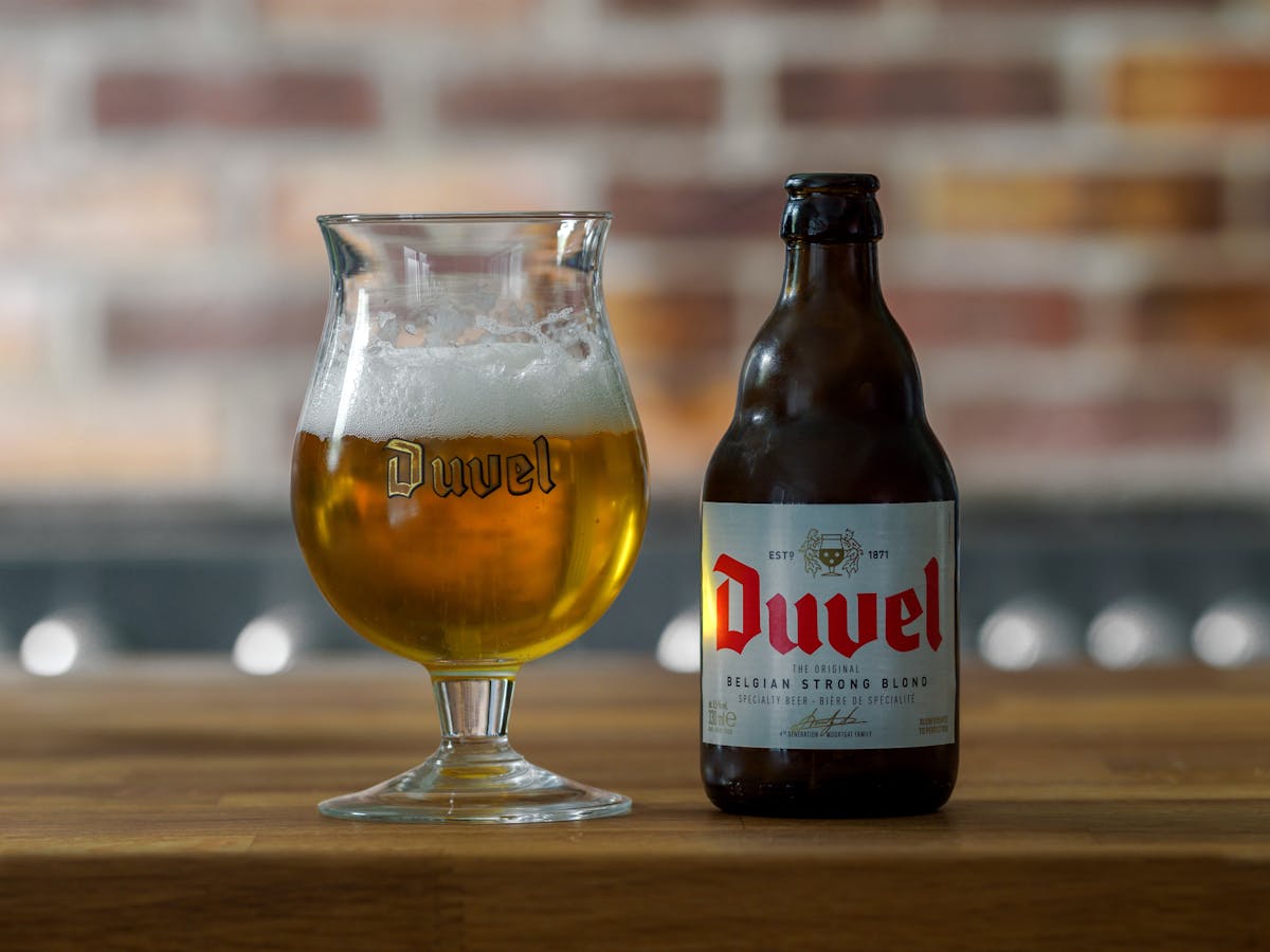 Glass of Belgian Trappist beer poured next to a brown bottle on a wooden table in a traditional Belgian pub