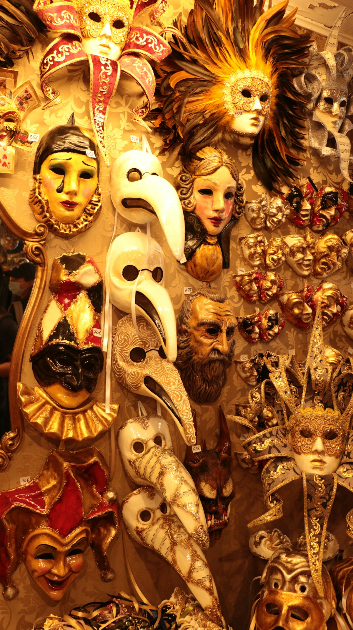 Wall display of ornate golden carnival masks with elaborate feathered headdresses and jester designs