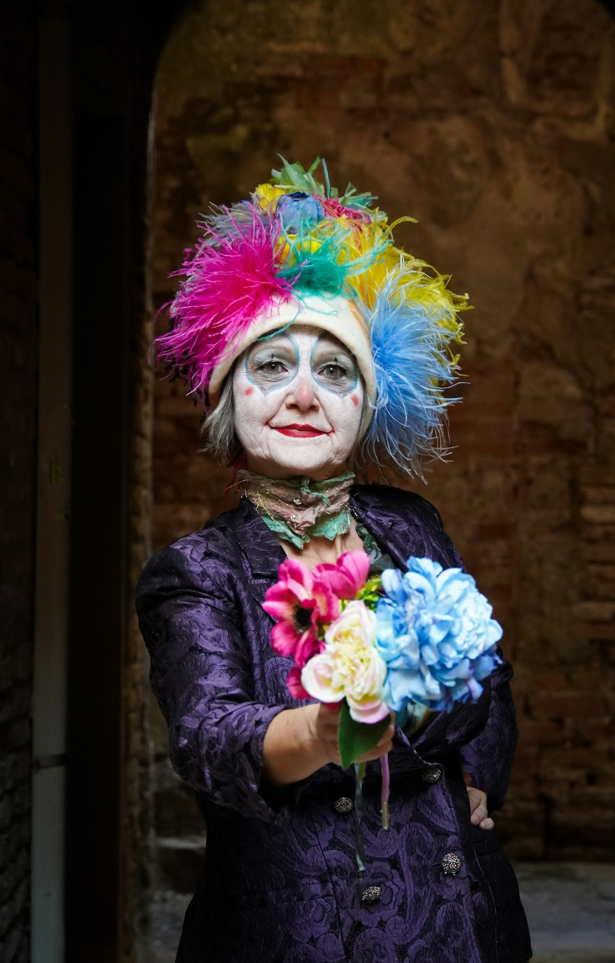 Carnival performer in colorful costume with face paint holding bouquet of vibrant flowers