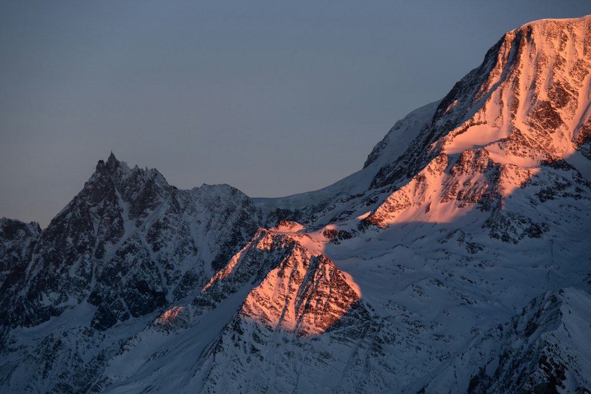 Sharp granite spires of the Mont Blanc massif catching orange alpenglow above a snowfield