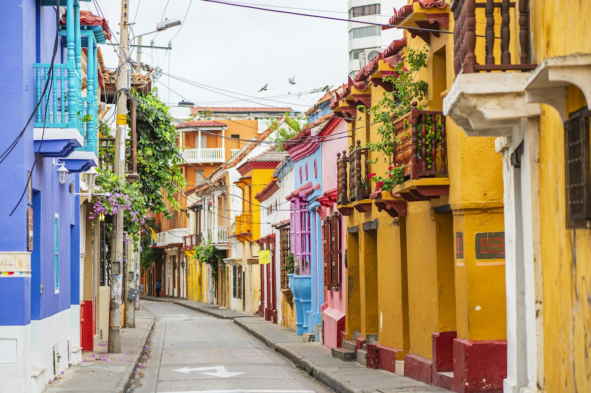 Narrow street in Cartagena's walled old town lined with pink, yellow and blue colonial houses with wooden balconies