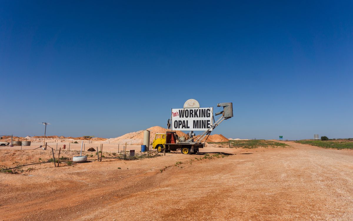 Working opal mine sign standing among red dirt mullock heaps in the Australian outback