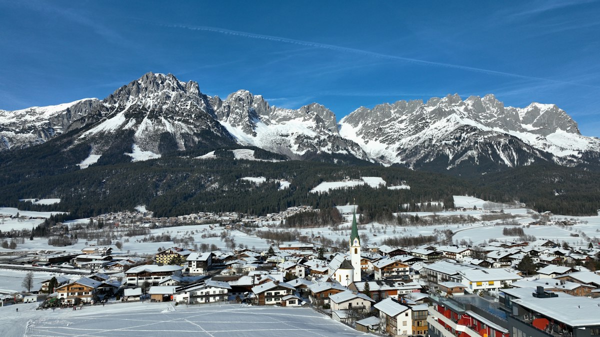Alpine town spread across a snowy valley floor beneath steep jagged limestone peaks