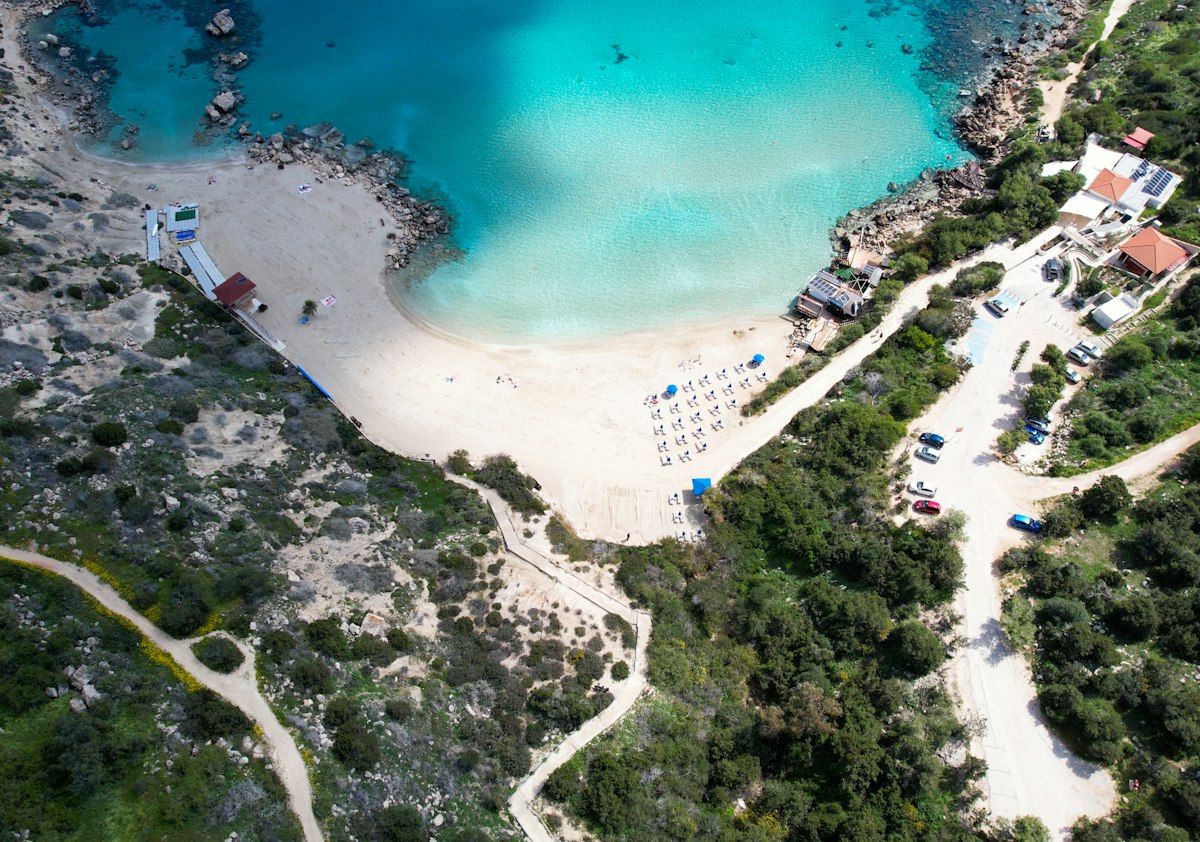 Aerial view of a turquoise cove in Cyprus with white sand, sun loungers and rocky headlands on both sides