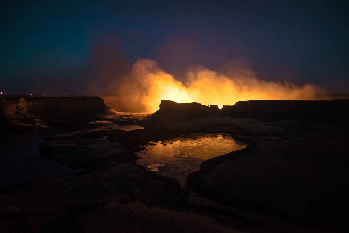 Orange flames glowing from a wide crater in the dark, lighting up the rocky ground around it