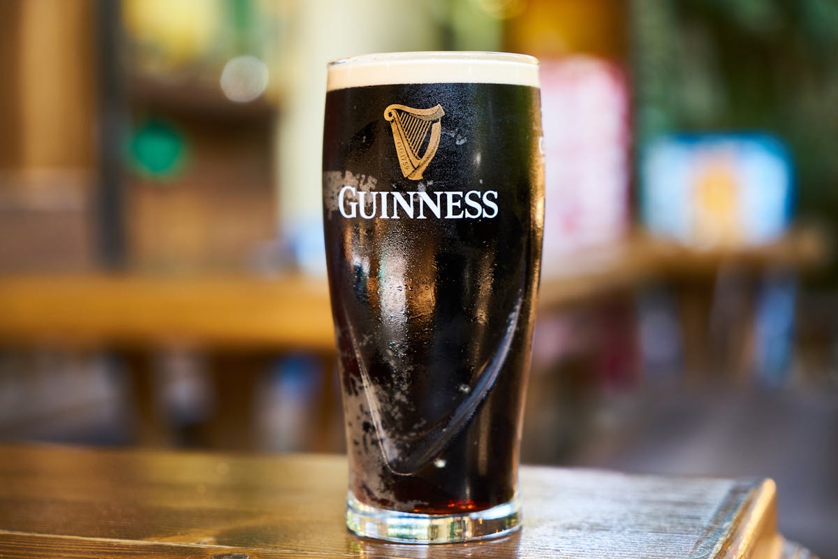Pint of Guinness stout with thick creamy white head settling on a wooden bar table in a traditional Dublin pub
