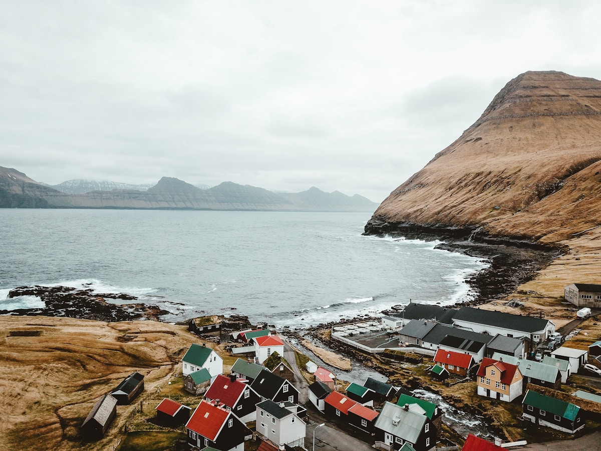 Colorful houses clustered along the rocky coastline of a Faroese village with mountains and overcast sky