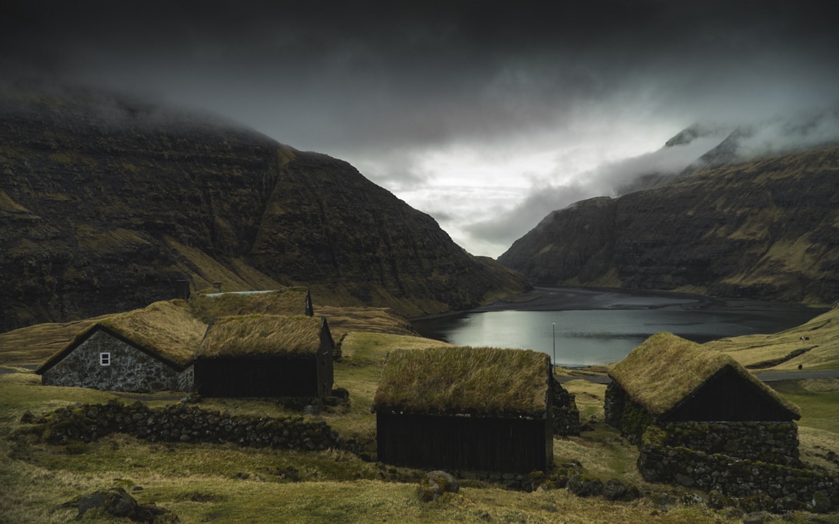 Traditional grass-roofed stone houses in Saksun village with a fjord and dramatic mountains in the background