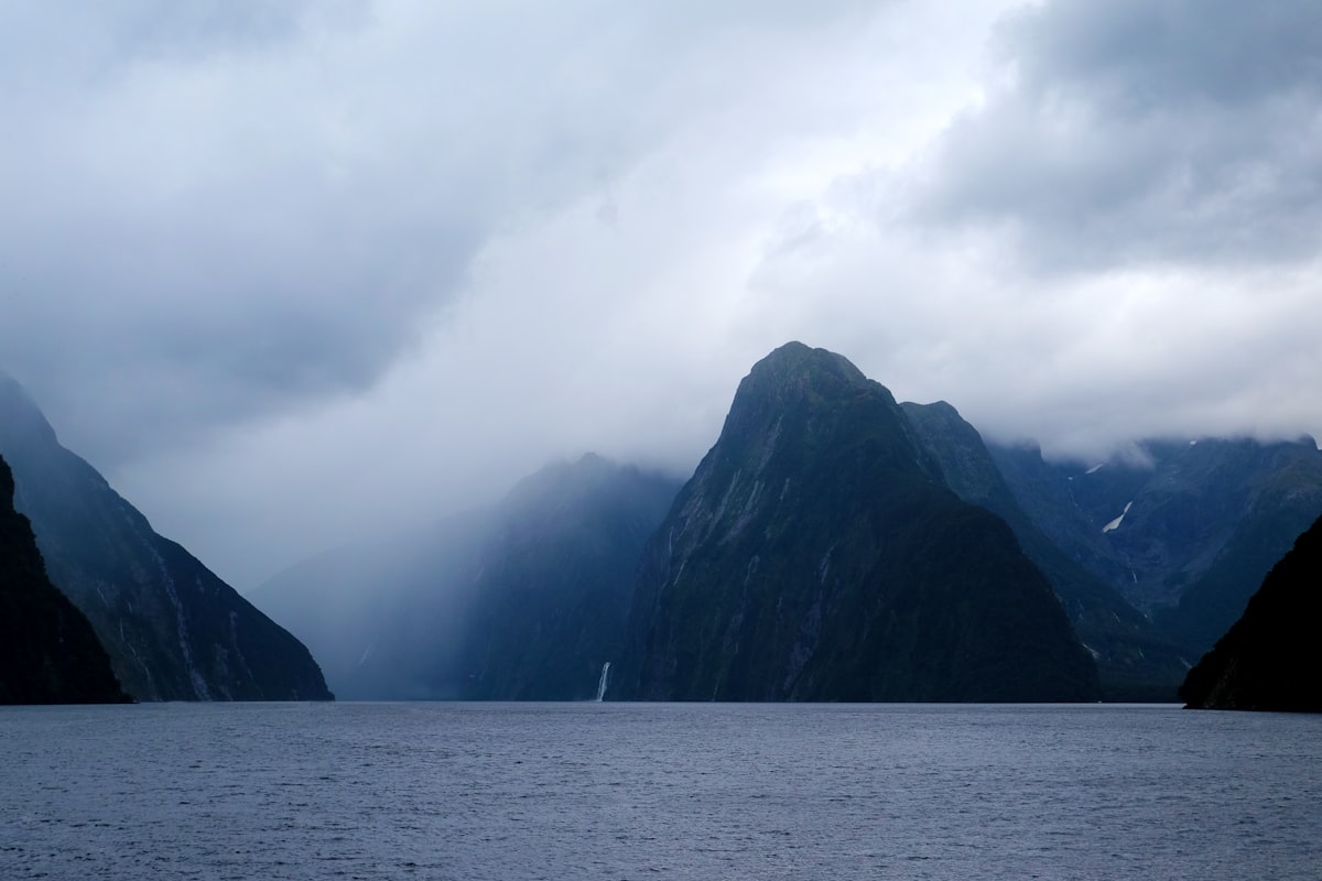Misty peaks of Milford Sound rising above dark waters in Fiordland National Park, New Zealand