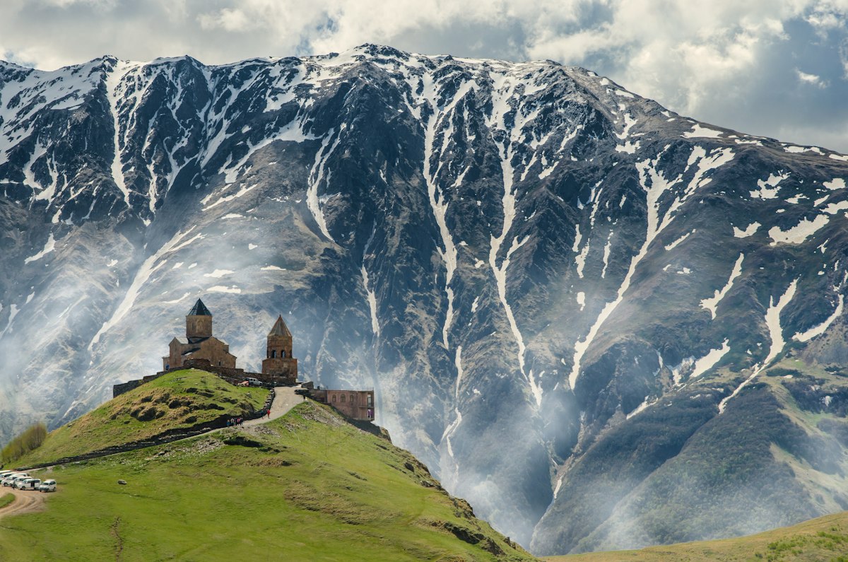 Gergeti Trinity Church standing alone on a green hill below the snow-covered slopes of Mount Kazbek in the Caucasus