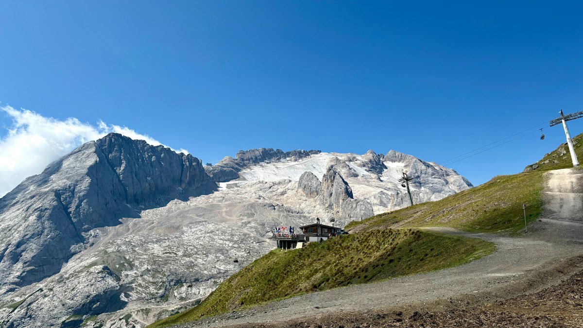 Summer glacier above green alpine slopes with a mountain lodge and lift line running up the rock