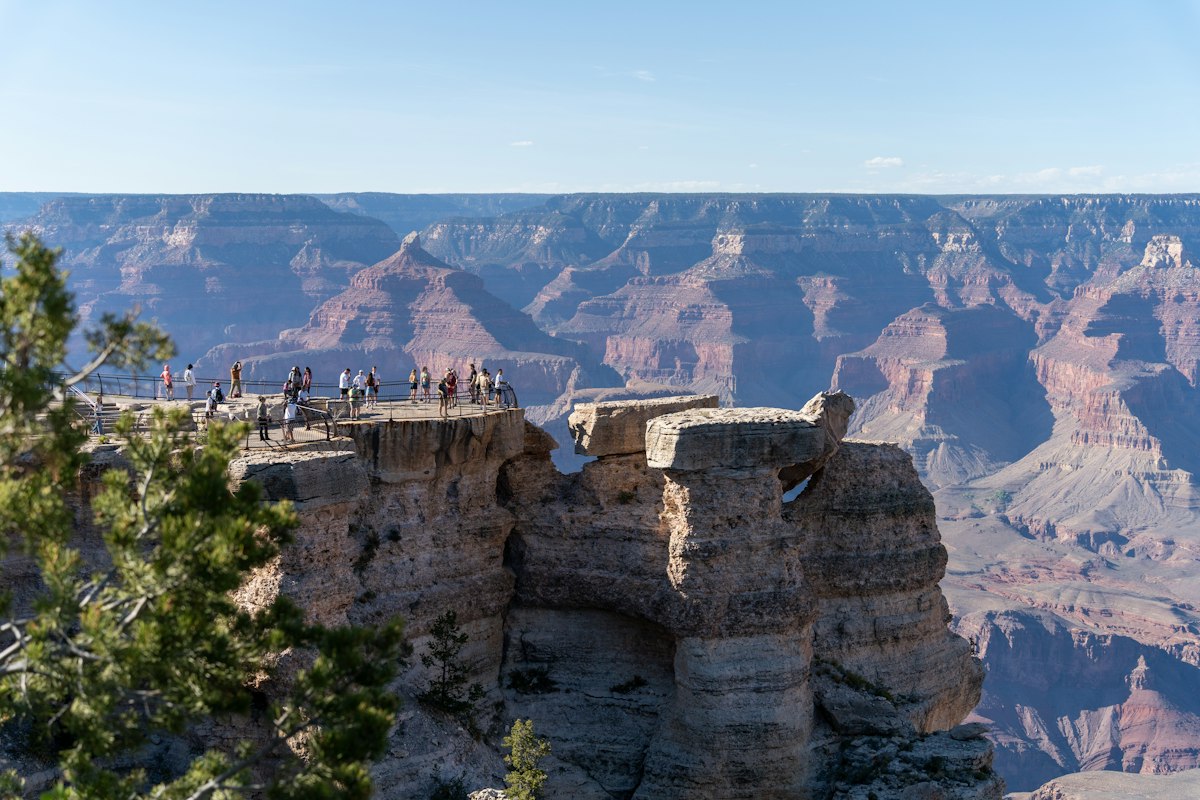 Visitors standing at a rocky overlook above the layered red walls of the Grand Canyon
