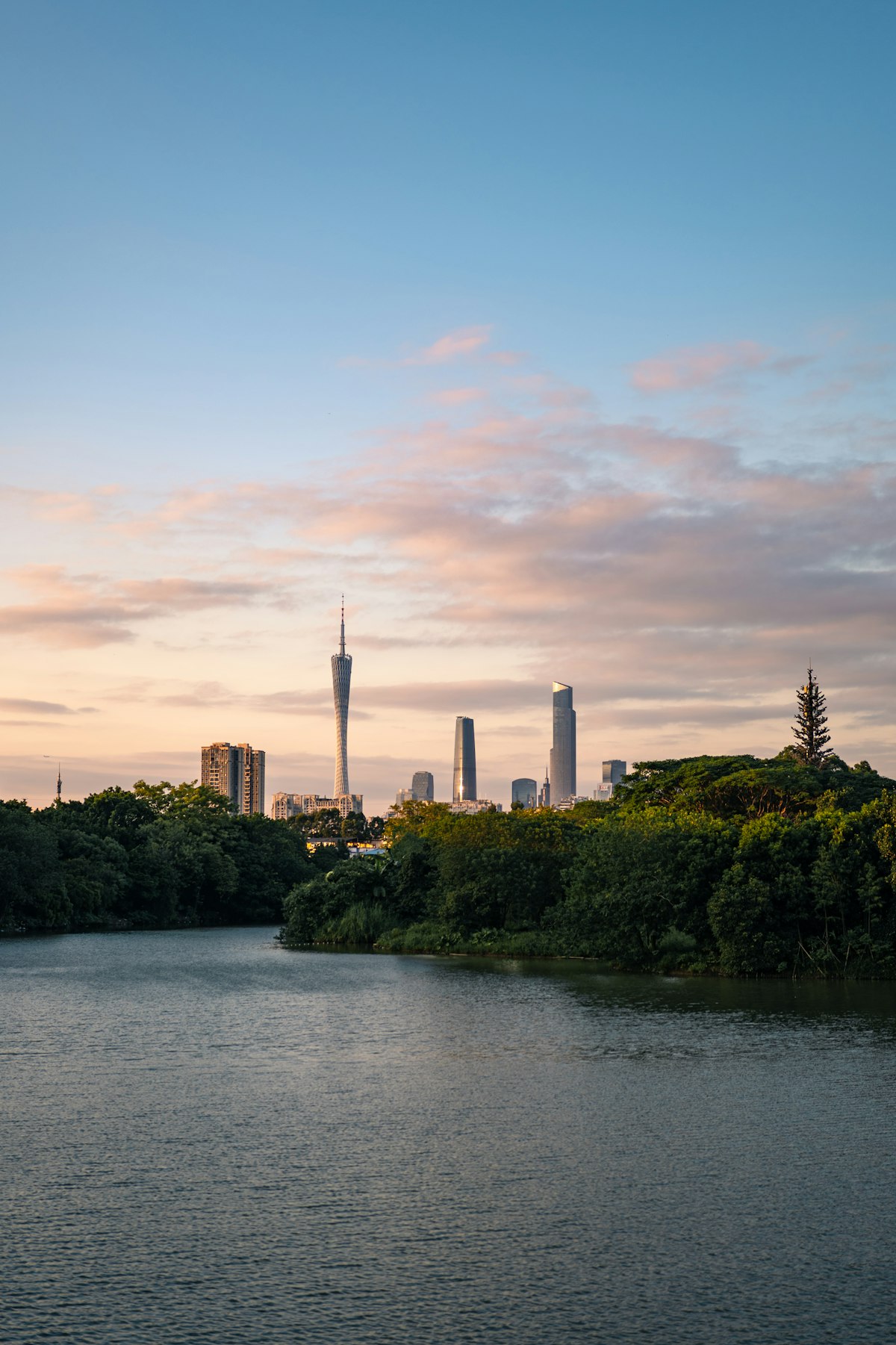 Pearl River waterfront promenade in Guangzhou with modern skyscrapers and traditional boats at sunset