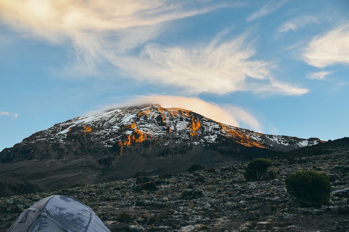 Tent at a Kilimanjaro camp with the snow-covered Kibo peak glowing at sunset in the background