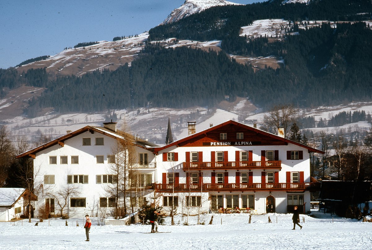 Traditional Tyrolean guesthouse with red shutters standing in snow below a forested mountain