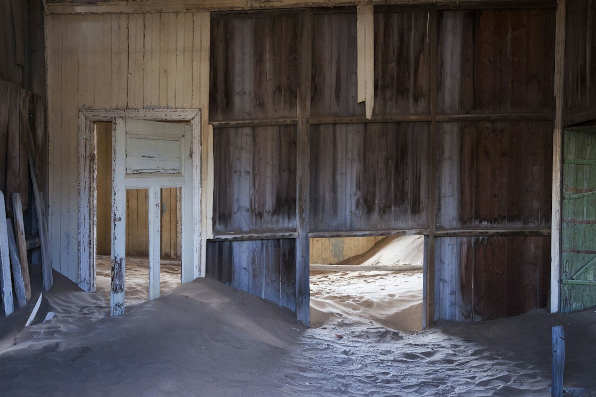 Abandoned room in a derelict house with desert sand pouring through a doorway and filling the floor