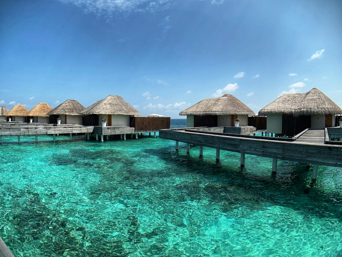 Row of thatched overwater villas on stilts above clear turquoise water in the Maldives