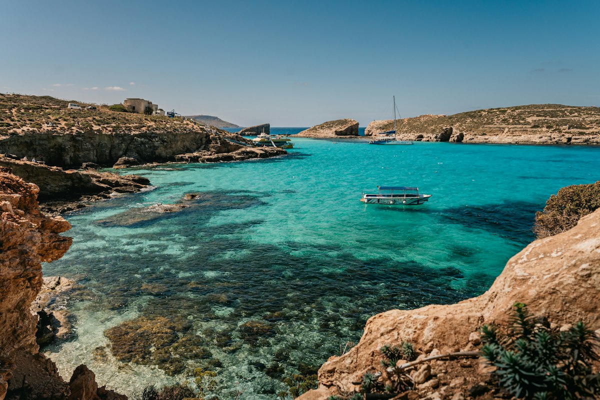 Boats floating on the bright turquoise water of Malta's Blue Lagoon between low rocky cliffs