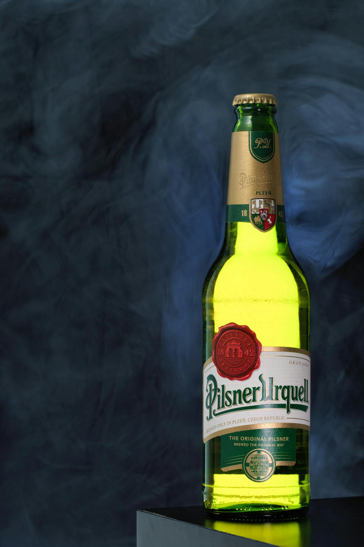 Bottle of Pilsner Urquell beer photographed against a textured smoky background showcasing the iconic Czech lager brand