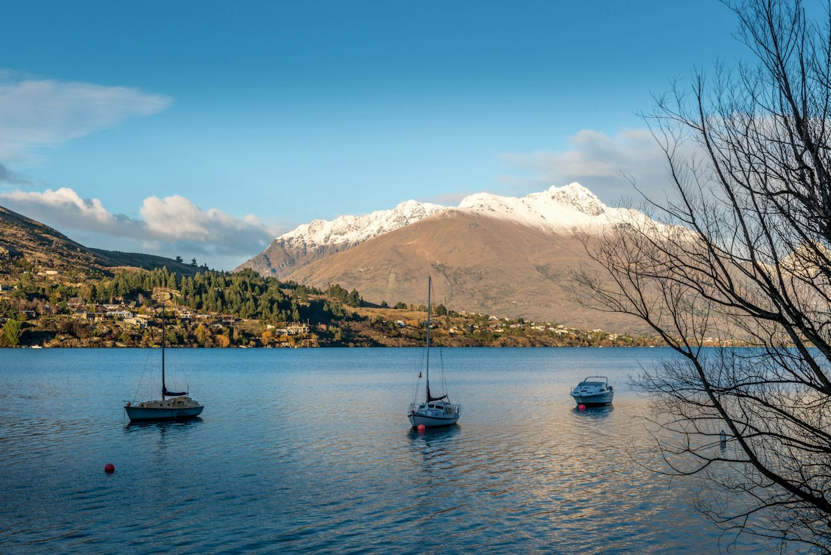 Sailboats moored on a calm lake below snow covered peaks in the New Zealand winter