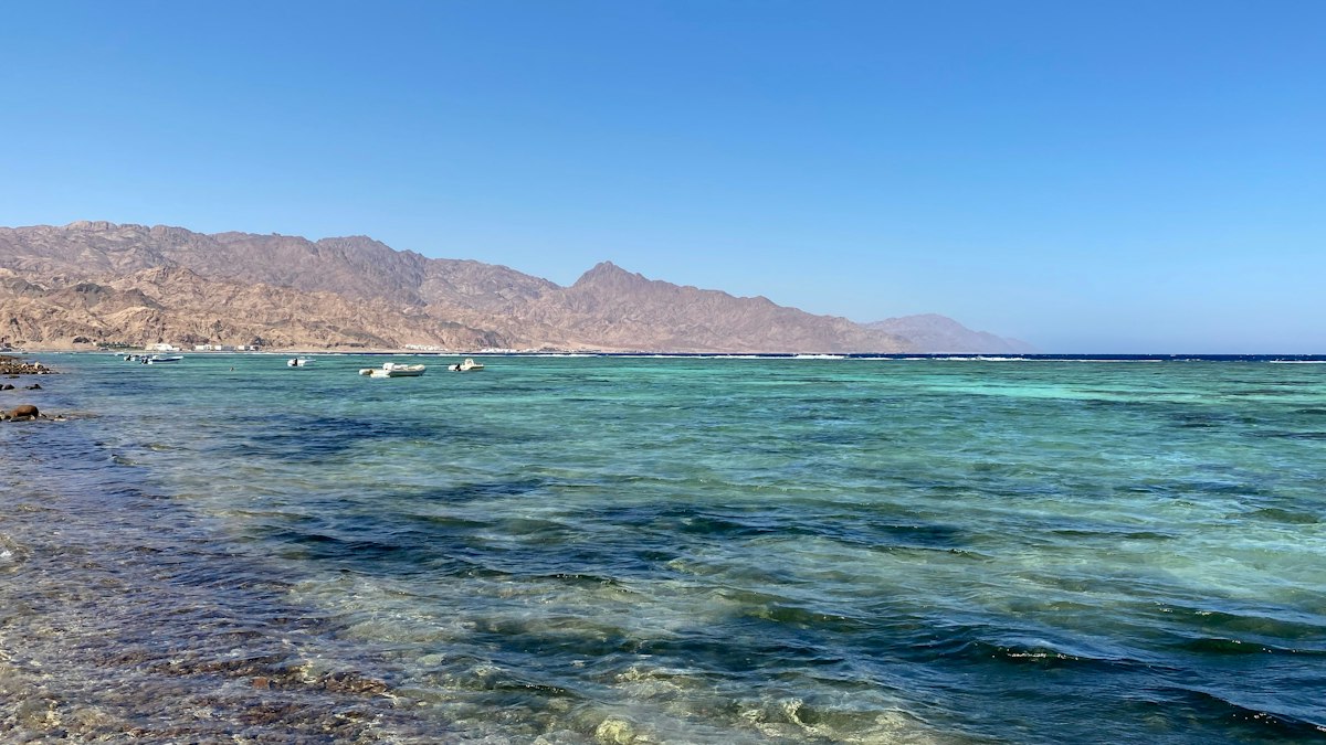 Shallow turquoise reef water along the Red Sea coast with bare desert mountains rising in the background