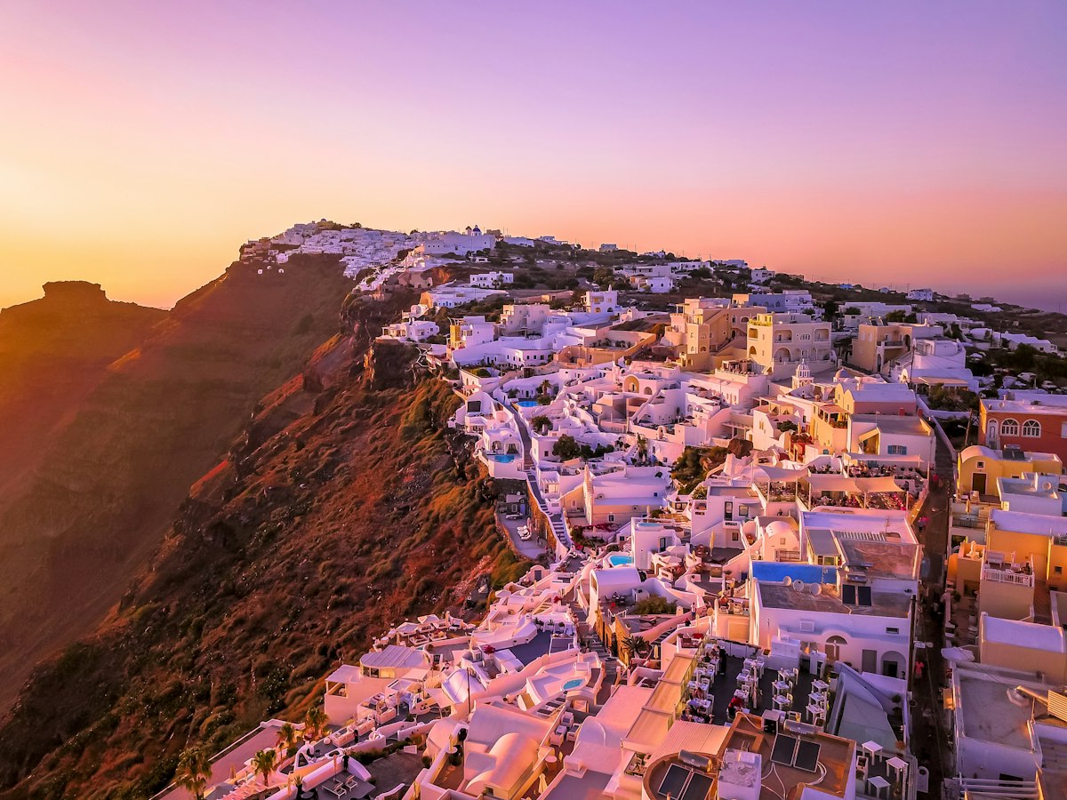 White cubic houses and blue domes of Oia stacked along the Santorini caldera rim in pink sunset light