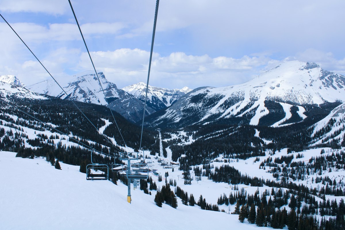 Chairlift cables strung across a snow covered valley with forested slopes below