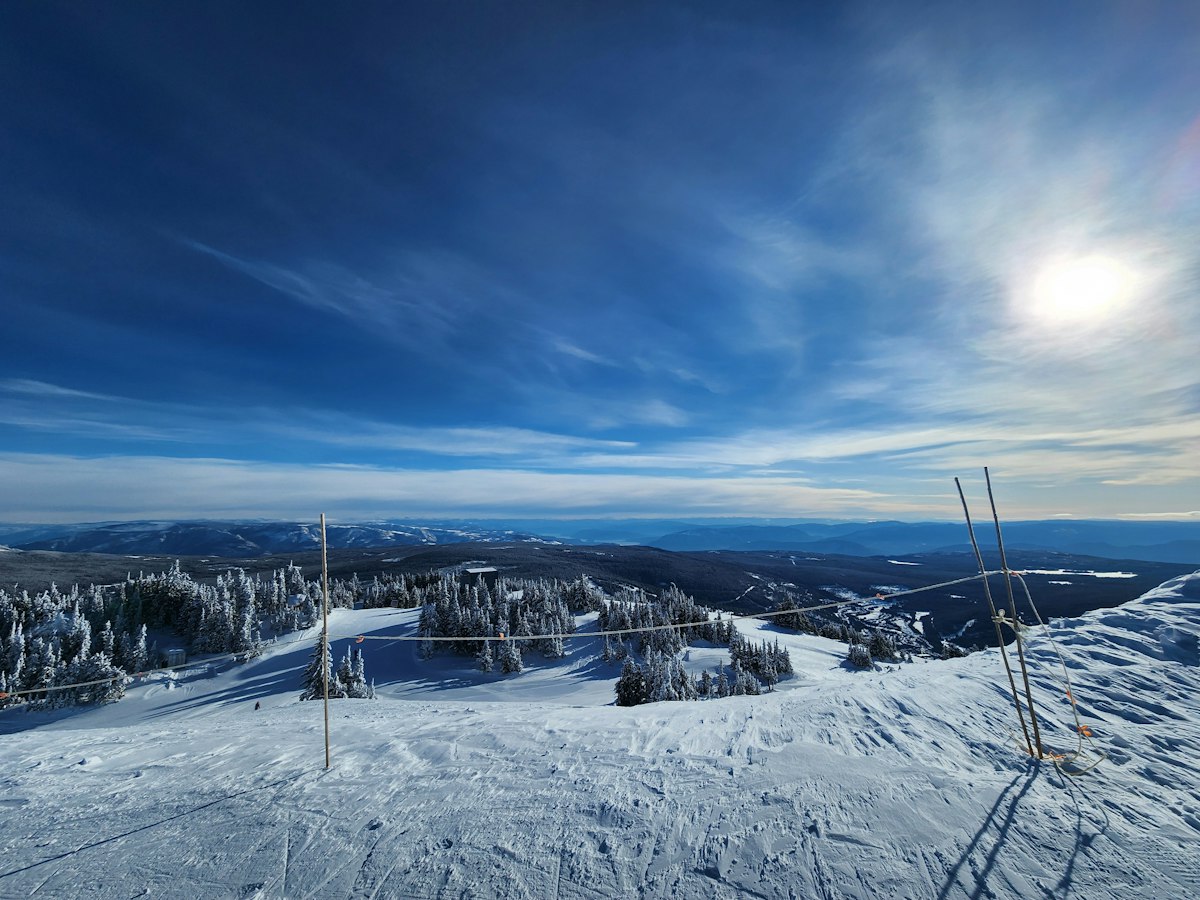 Wide snowy ski slope under a bright sun with distant peaks on the horizon