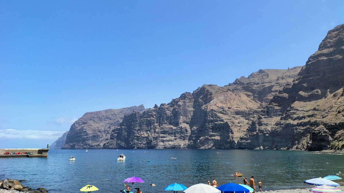 Beach with colorful umbrellas at the foot of the towering Los Gigantes cliffs on Tenerife