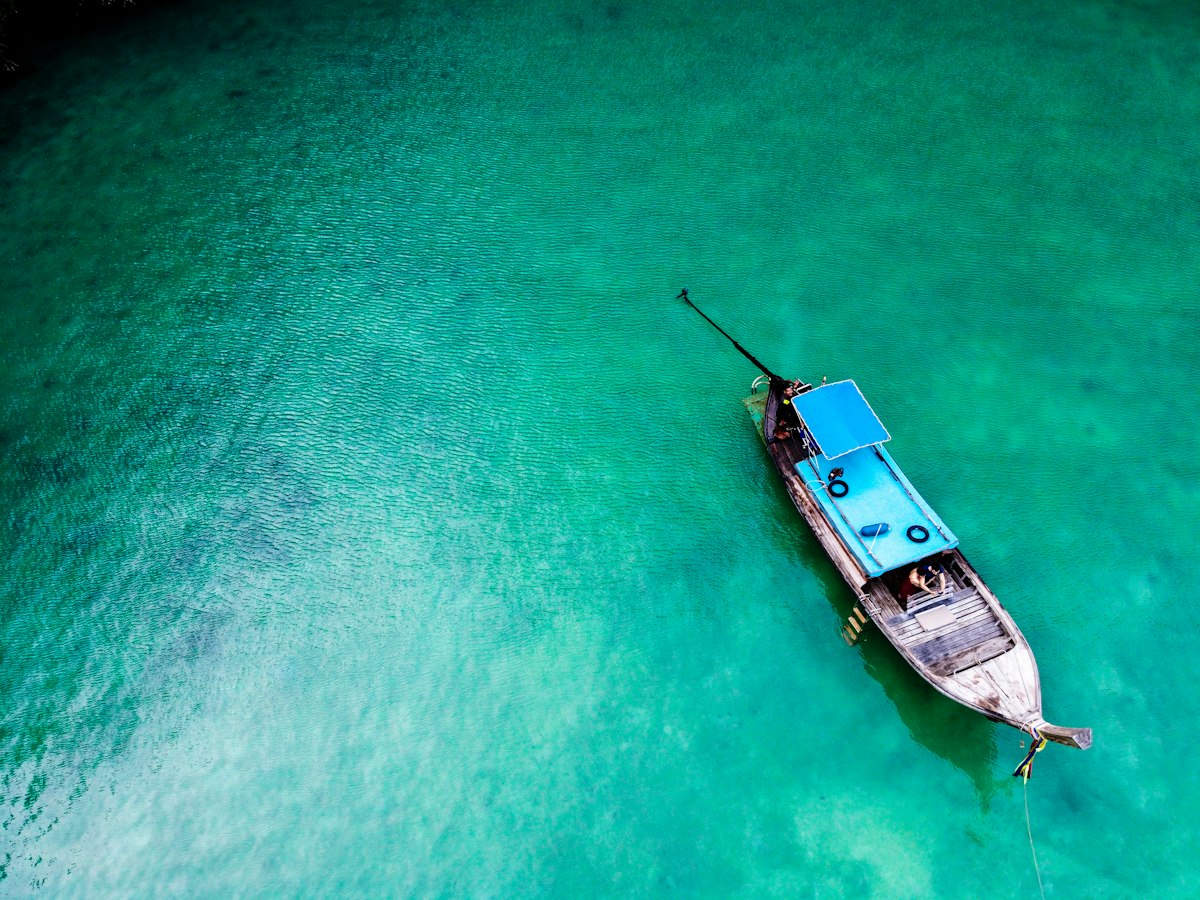 Aerial view of a wooden longtail boat anchored in bright turquoise shallows off a Thai island beach