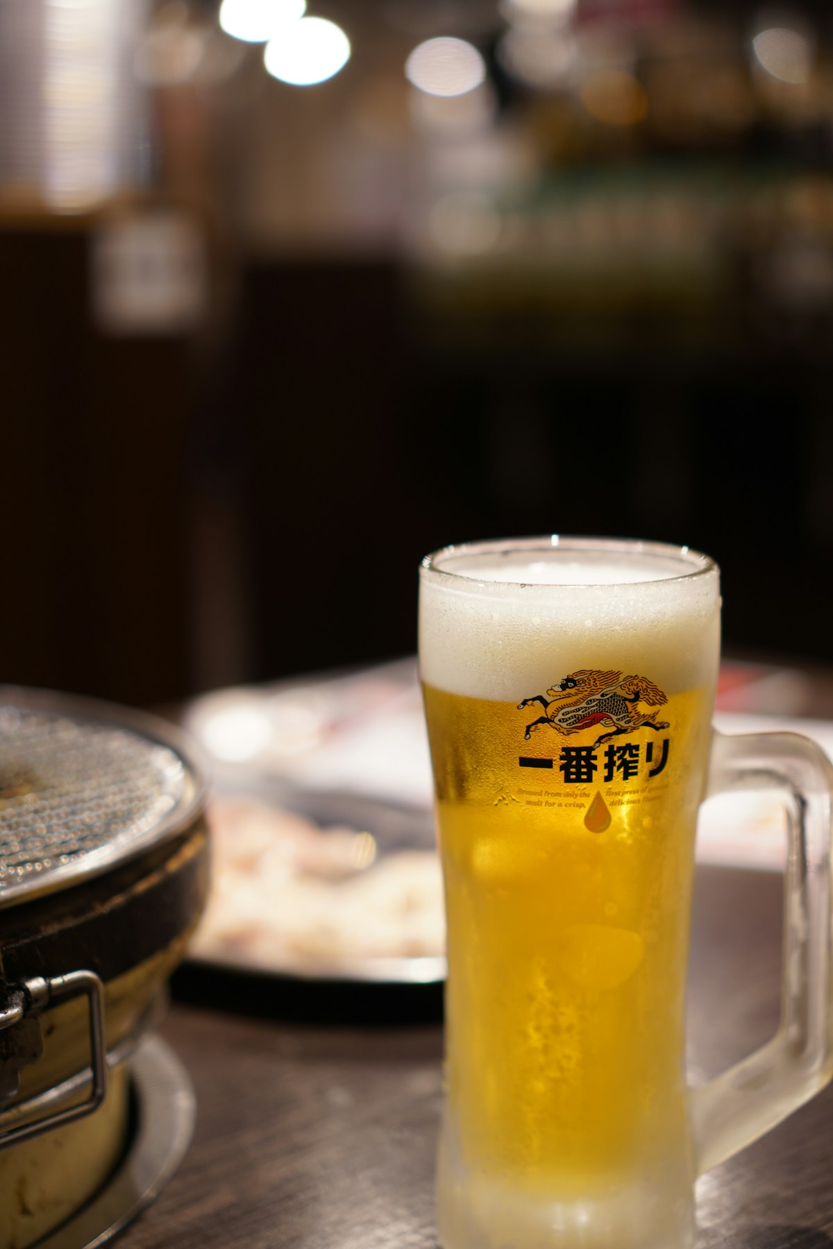 Glass of golden Japanese craft beer with foam head sitting on a wooden table in a small Tokyo izakaya