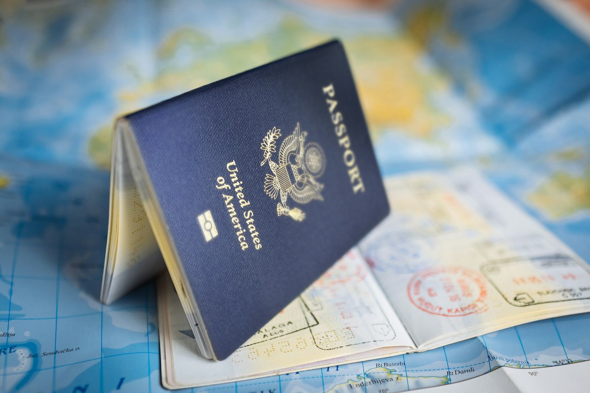 Open passport filled with entry stamps resting on a colorful world map next to travel documents