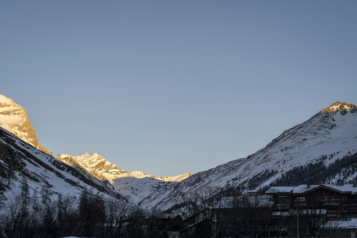 Snow covered valley and ski slopes glowing in low sunlight with mountain peaks in the background