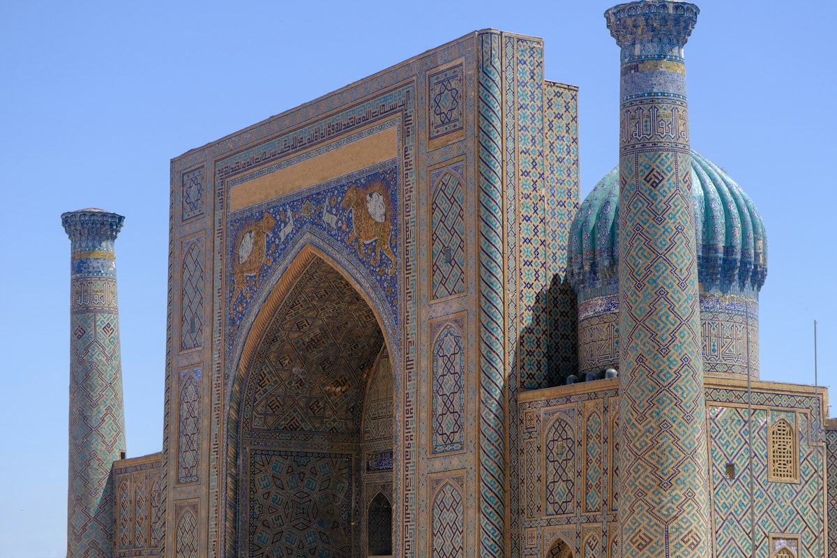 Tiled blue facade and minarets of a madrasa on Registan square in Samarkand under a clear sky