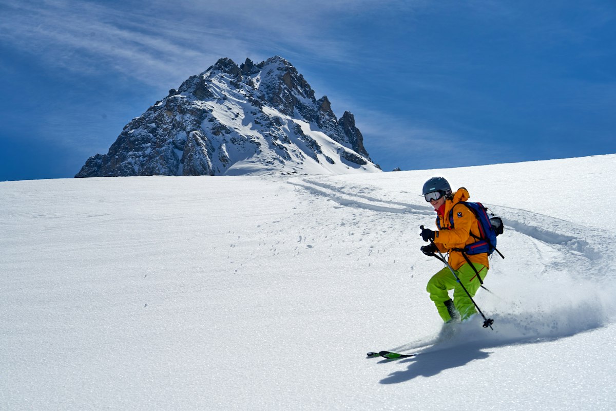 Skier in an orange jacket carving through fresh powder snow on an open mountain slope