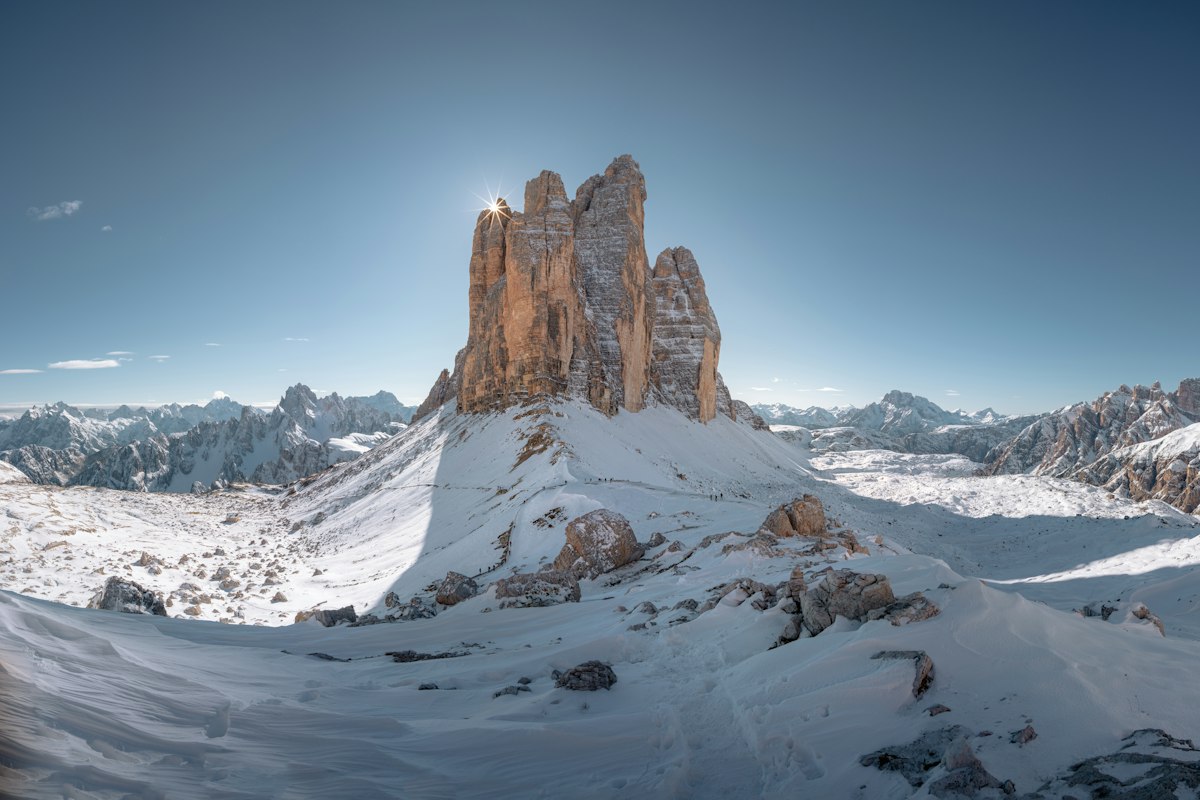 Jagged pale rock towers of the Dolomites rising above snow covered slopes under a clear sky