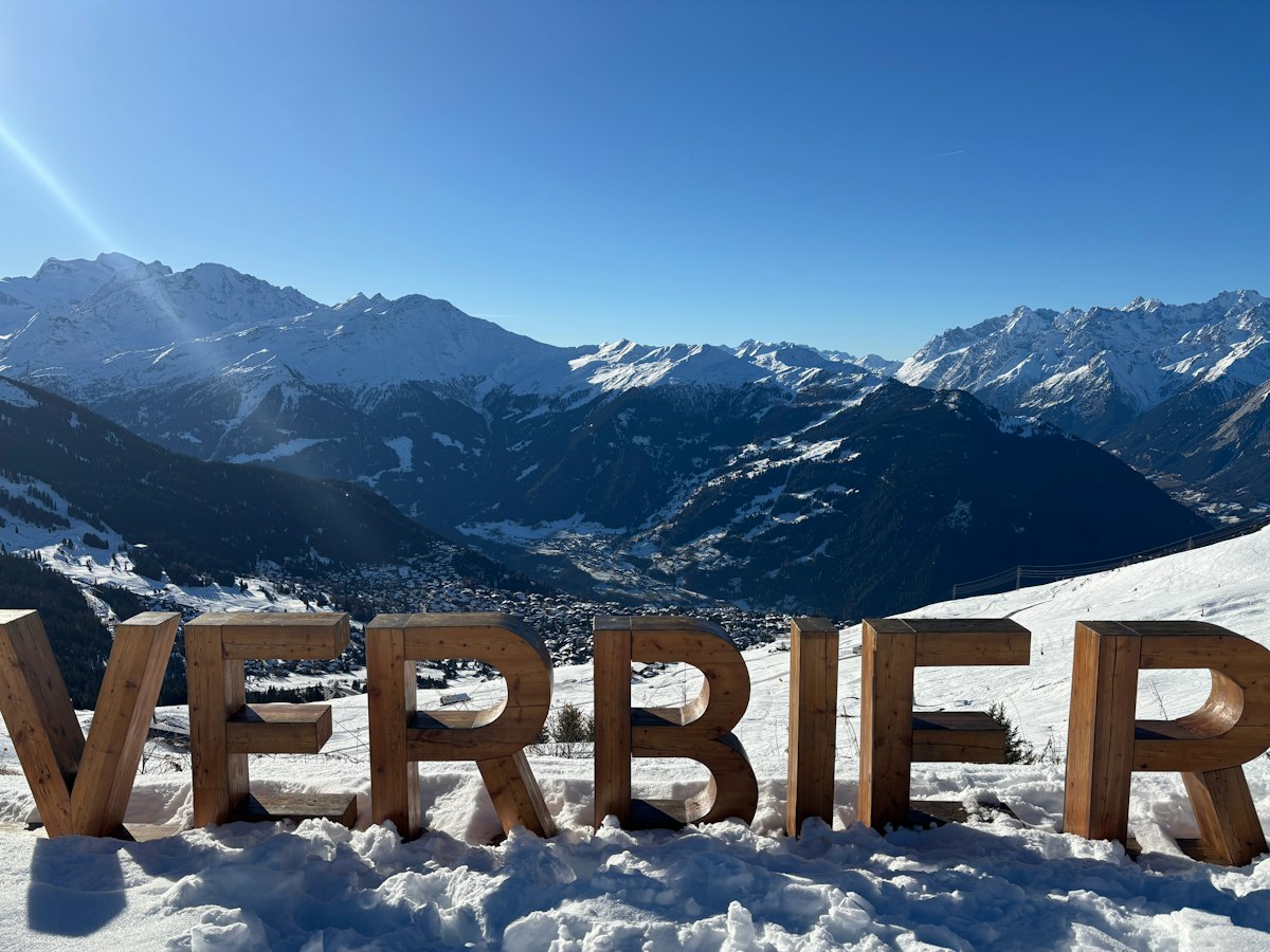 Large wooden letters spelling Verbier standing in the snow above a wide alpine valley