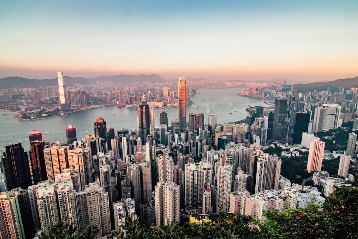 Dense cluster of Hong Kong skyscrapers along Victoria Harbour seen from high above at dusk